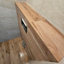 Dariusz Zambrzycki DMM Usługi Glazurnicze - Wykończona łazienka z drewnopodobnymi płytkami na podłodze i ścianach, zabudowa WC z ukrytym stelażem. Widoczne fugi i fragment stopy. Ujęcie z góry.