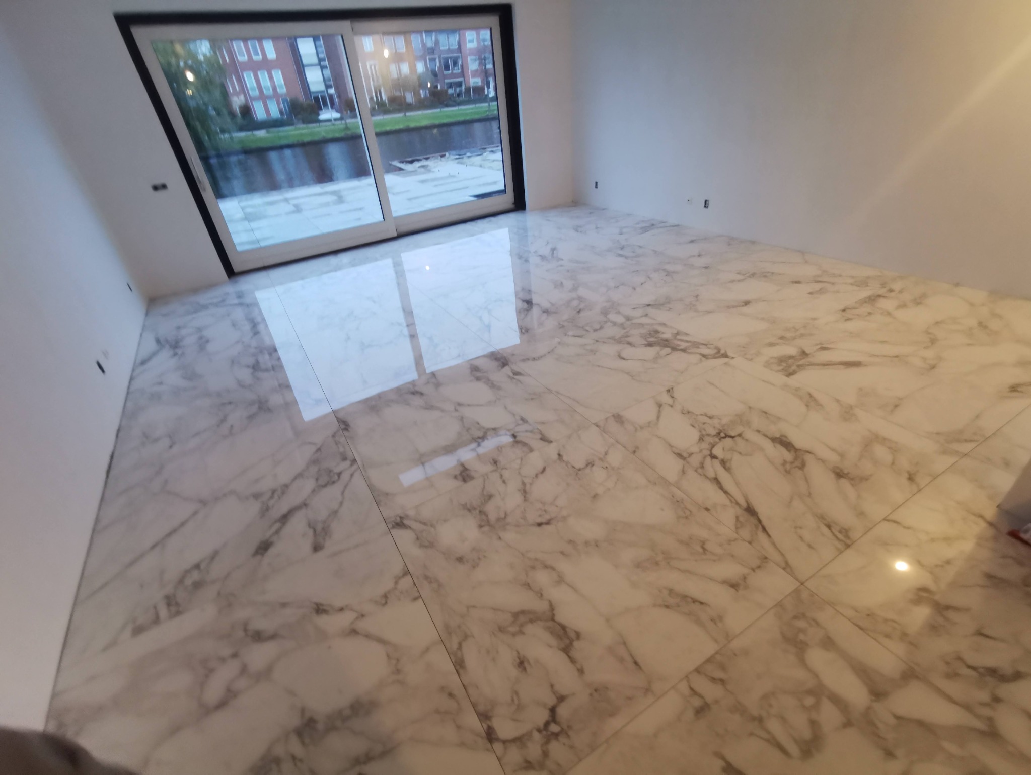 Biała marmurowa podłoga z szarymi żyłami, widok na okno przesuwne z widokiem na kanał i budynki.
