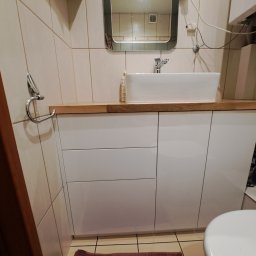 SZPAK MEBLE - Nowoczesna łazienka z białą szafką pod umywalką z drewnianym blatem, prostokątną umywalką nablatową i lustrem w metalowej ramie.