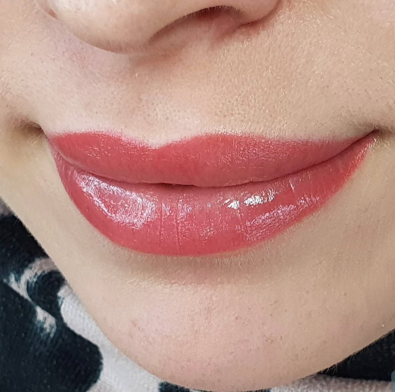Zbliżenie na usta z makijażem permanentnym, widoczny błyszczący, koralowy kolor i precyzyjny kontur.