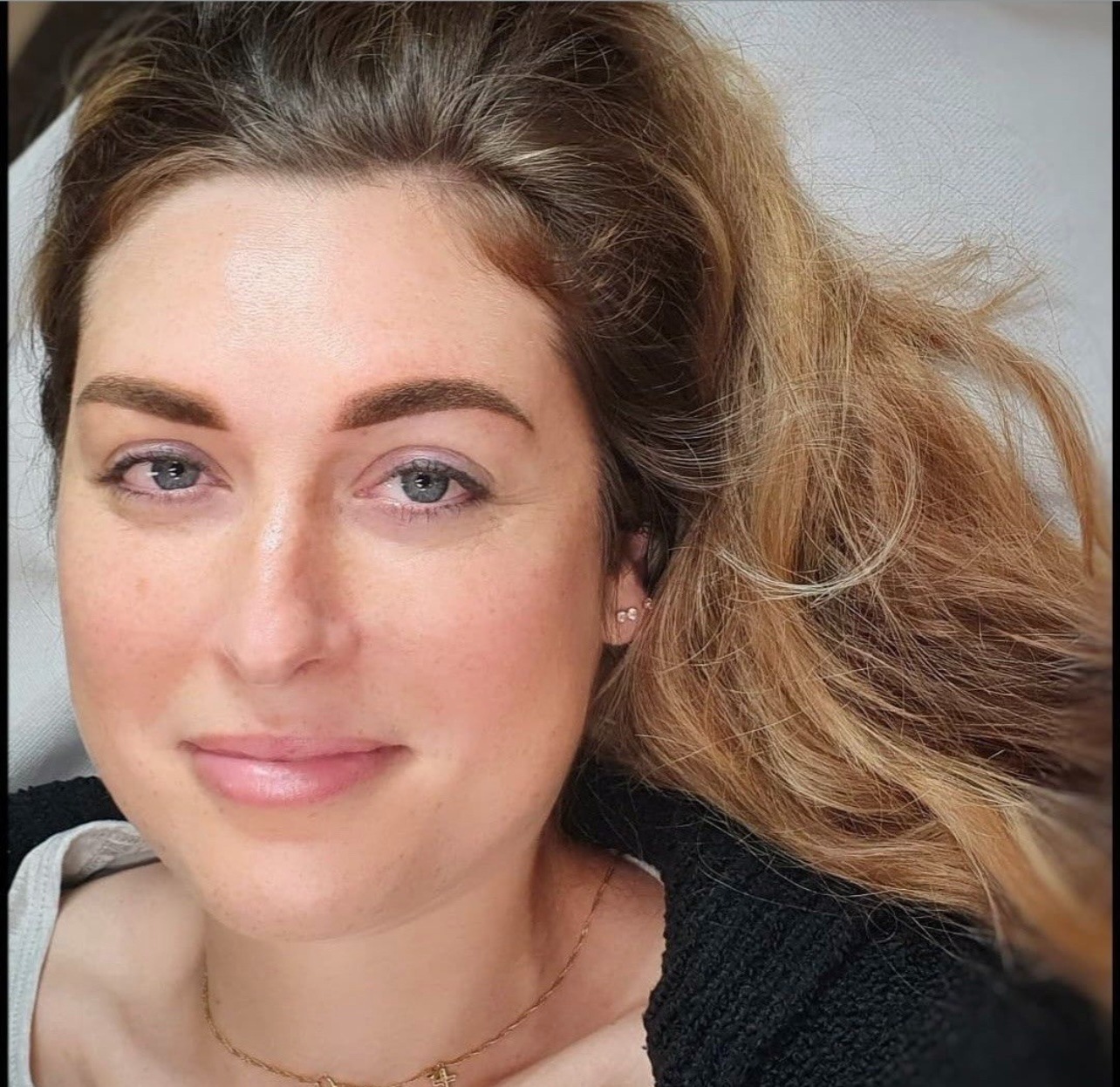 Portret kobiety z widocznymi brwiami po zabiegu pigmentacji, leżącej na białym podłożu, z blond włosami i delikatnym makijażem.