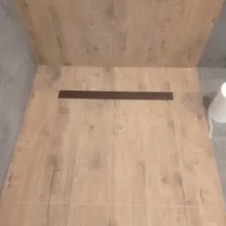 Wykończona podłoga w kabinie prysznicowej z odpływem liniowym, płytki imitujące drewno, szara ściana w tle.