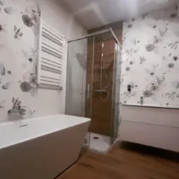 Nowoczesna łazienka z kabiną prysznicową z brązowym wykończeniem, białą wanną wolnostojącą i grzejnikiem drabinkowym na ścianie w kwiatowy wzór.