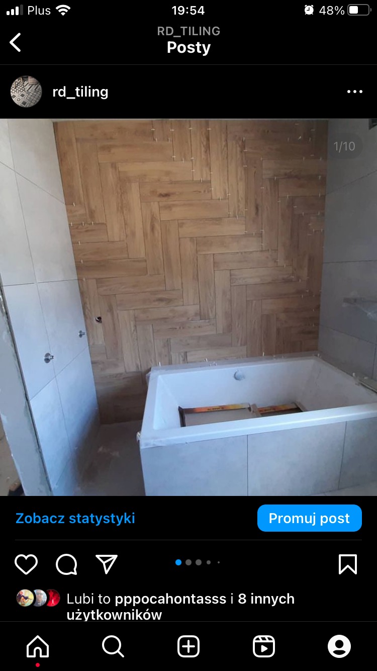 Łazienka w trakcie wykańczania: drewnopodobna glazura ułożona w jodełkę na ścianie nad wanną, widoczne krzyżyki dystansowe, częściowo wykończona obudowa wanny z płytek.