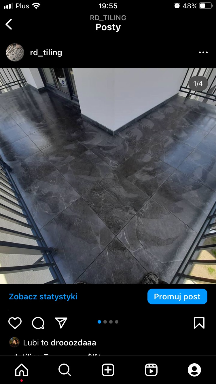 Błyszcząca, ciemna podłoga z płytek imitujących marmur, ułożona na balkonie, widoczna z góry, z fragmentem balustrady po lewej stronie.