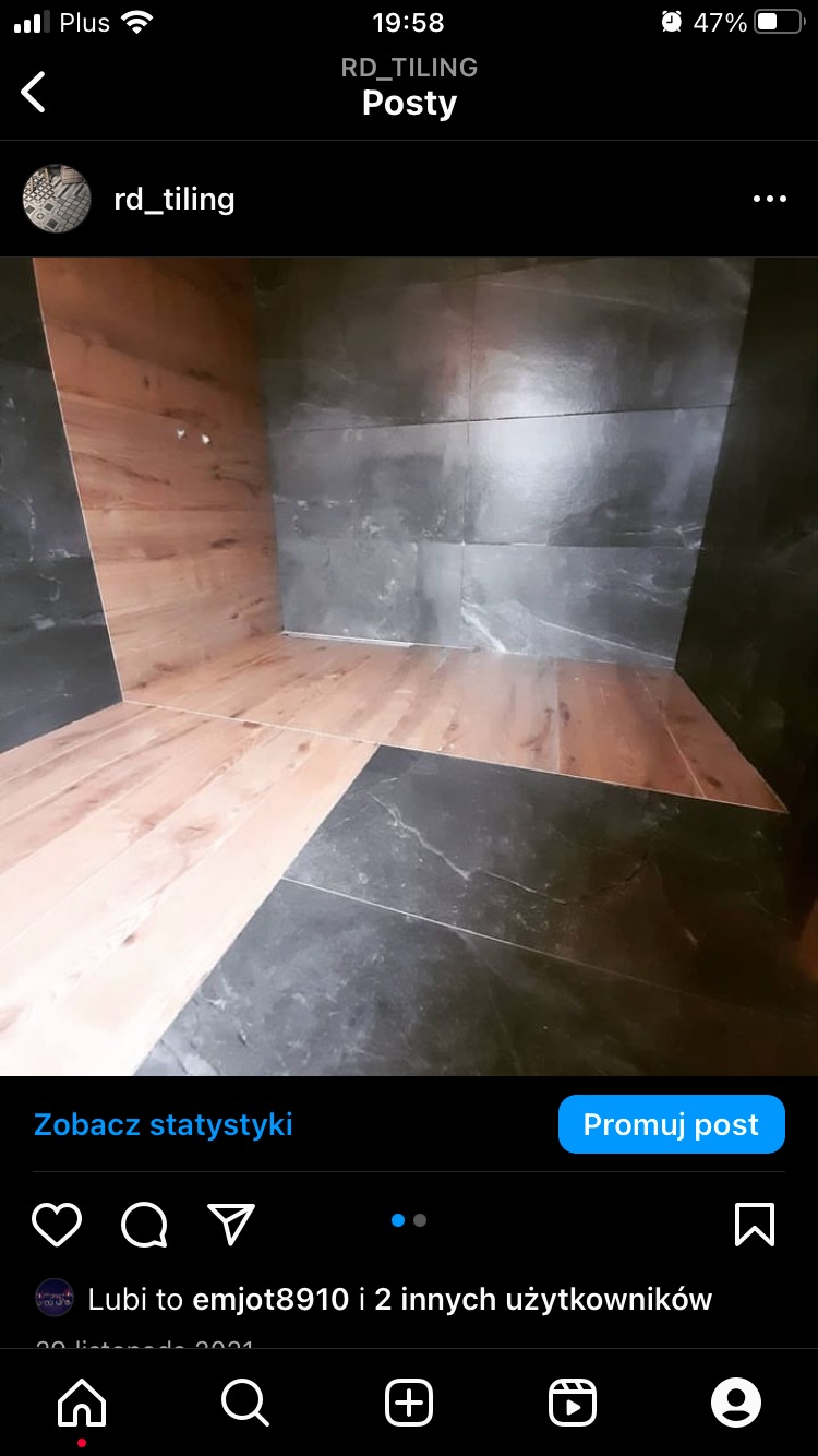 Wykończenie łazienki w Wieruszowie z kombinacją płytek imitujących drewno na ścianie i podłodze oraz ciemnych, marmurkowych płytek na pozostałych ścianach, tworzące nowoczesny design.