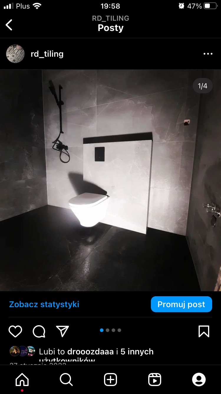 Nowoczesna łazienka z szarymi płytkami imitującymi marmur, wisząca toaleta z czarnym przyciskiem spłukującym i czarną armaturą prysznicową.