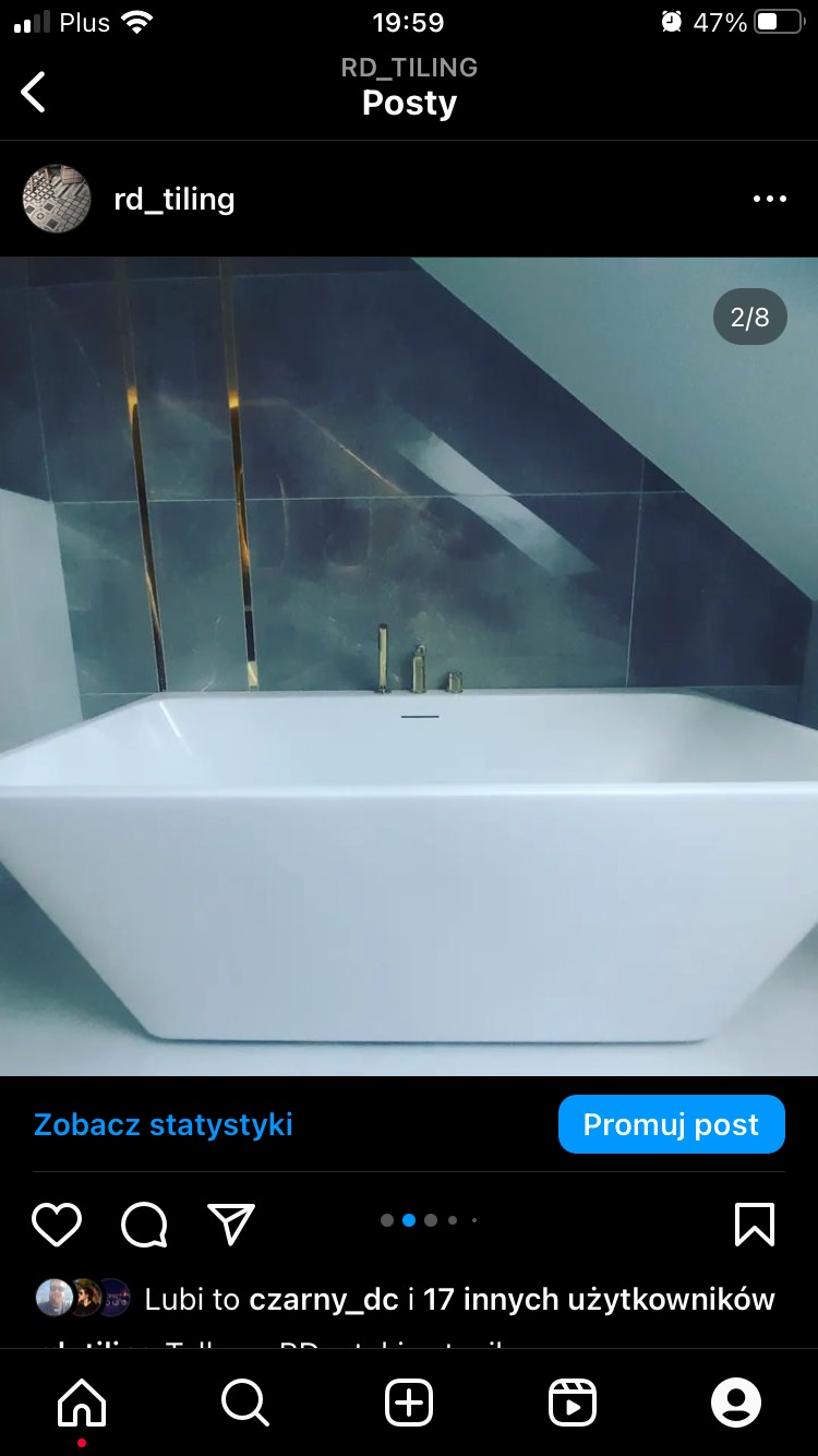 Biała, prostokątna wanna w łazience na poddaszu, z szarymi płytkami i złotymi akcentami, minimalistyczna armatura.