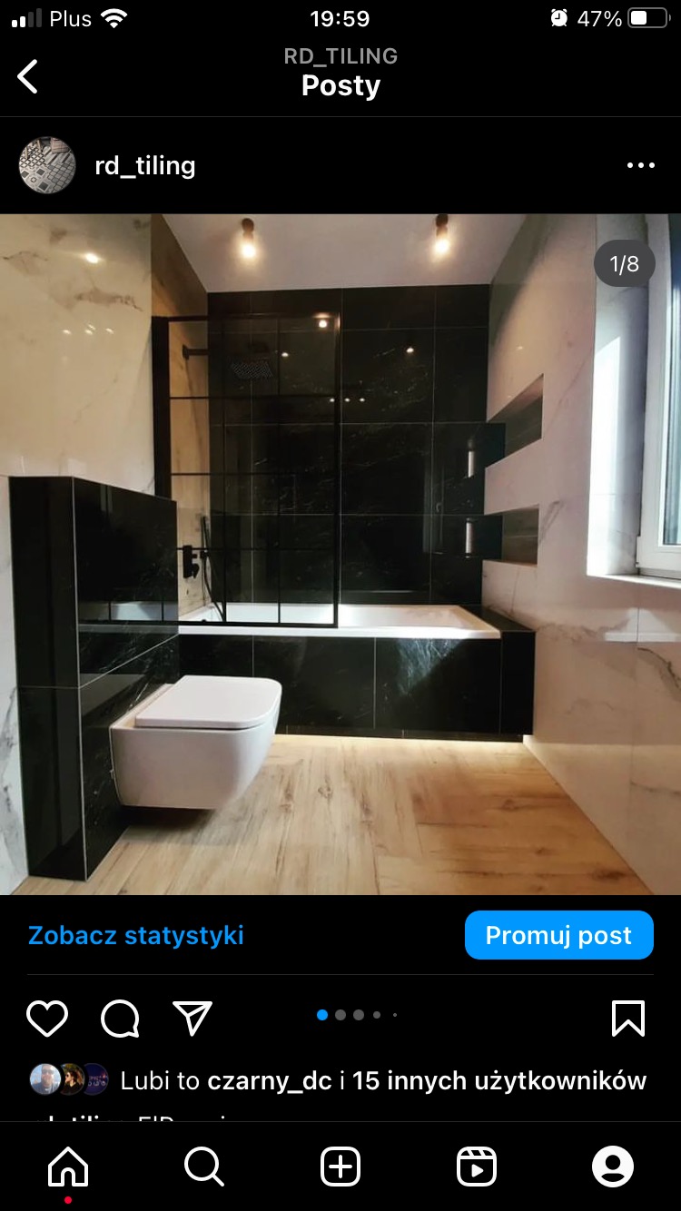 Nowoczesna łazienka z czarnymi płytkami imitującymi marmur, podwieszana toaleta i drewnopodobna podłoga z subtelnym oświetleniem LED