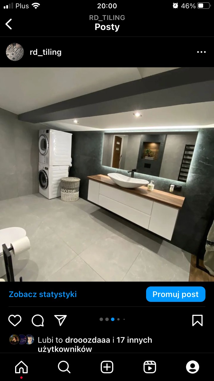 Nowoczesna łazienka w odcieniach szarości z pralką i suszarką w kolumnie, białą umywalką nablatową na drewnianym blacie, podświetlanym lustrem i szarymi płytkami na ścianach