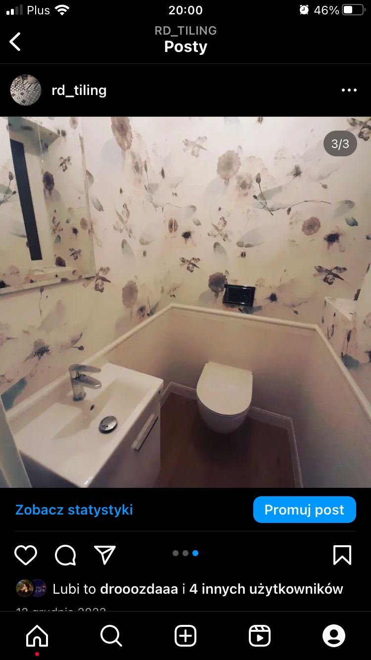 Mała łazienka po remoncie z toaletą typu Geberit i umywalką nablatową na szafce, ściany pokryte tapetą w kwiaty.