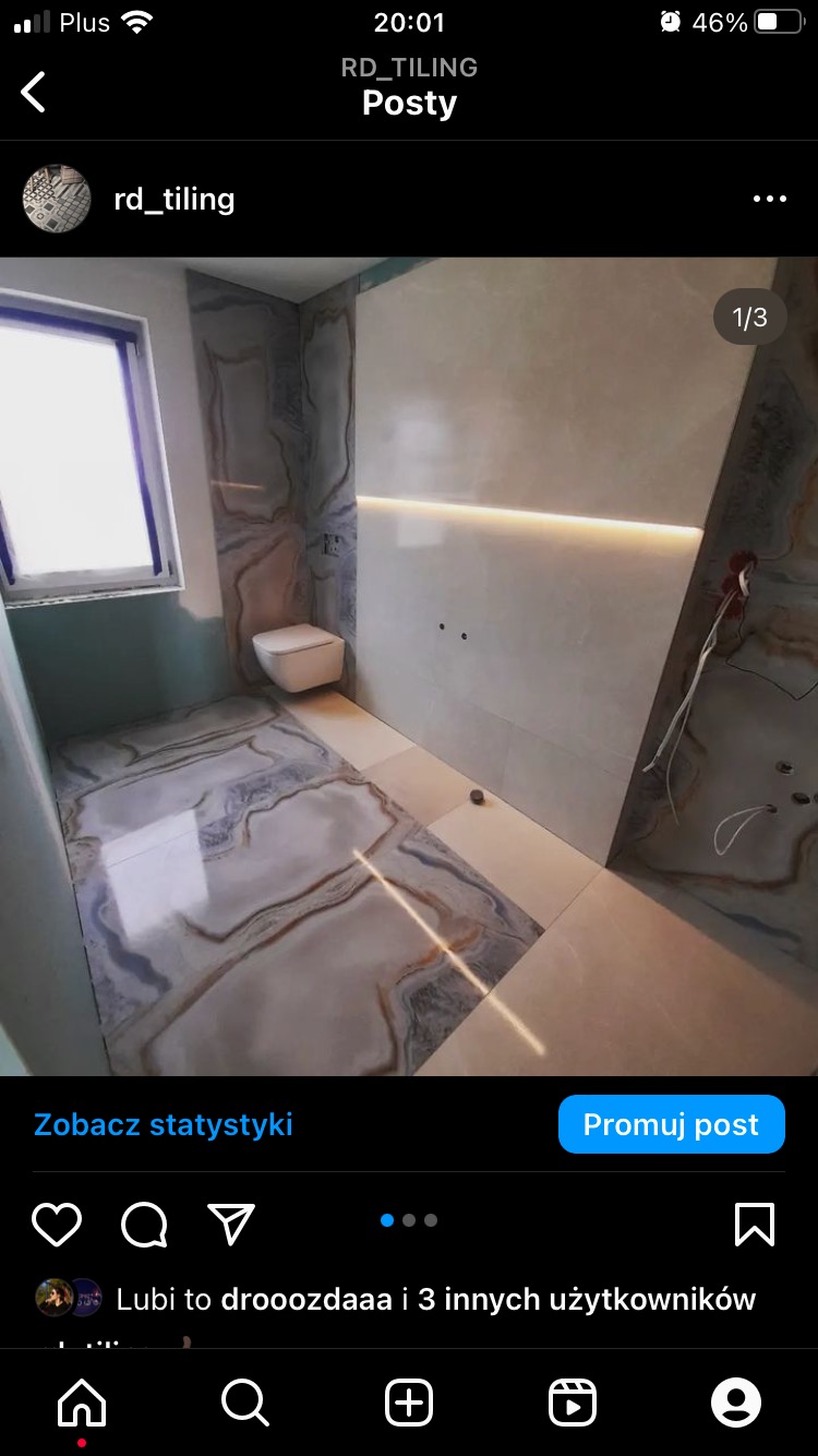 Nowoczesna łazienka z płytkami imitującymi marmur na podłodze i ścianach, podświetleniem LED nad toaletą podwieszaną i niedokończonymi instalacjami elektrycznymi.