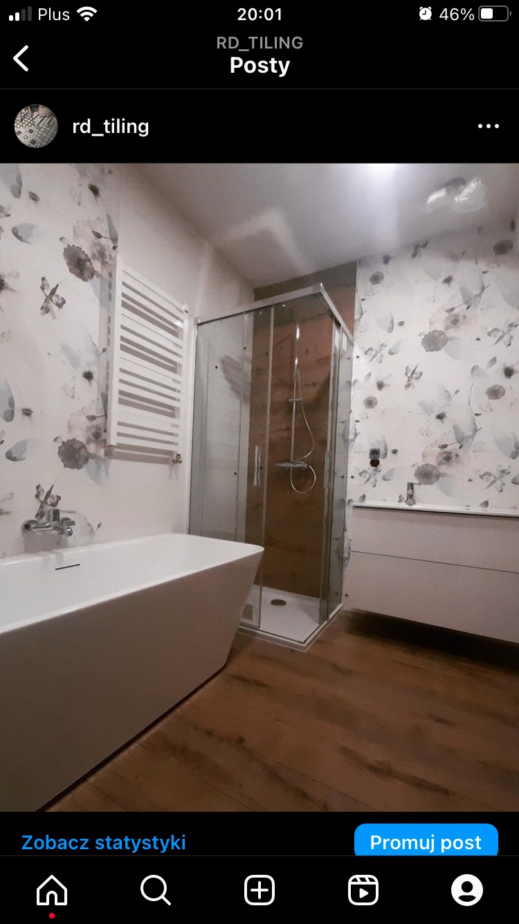 Nowoczesna łazienka z kabiną prysznicową z brązowym wykończeniem, białą wanną wolnostojącą i grzejnikiem drabinkowym na ścianie w kwiatowy wzór.