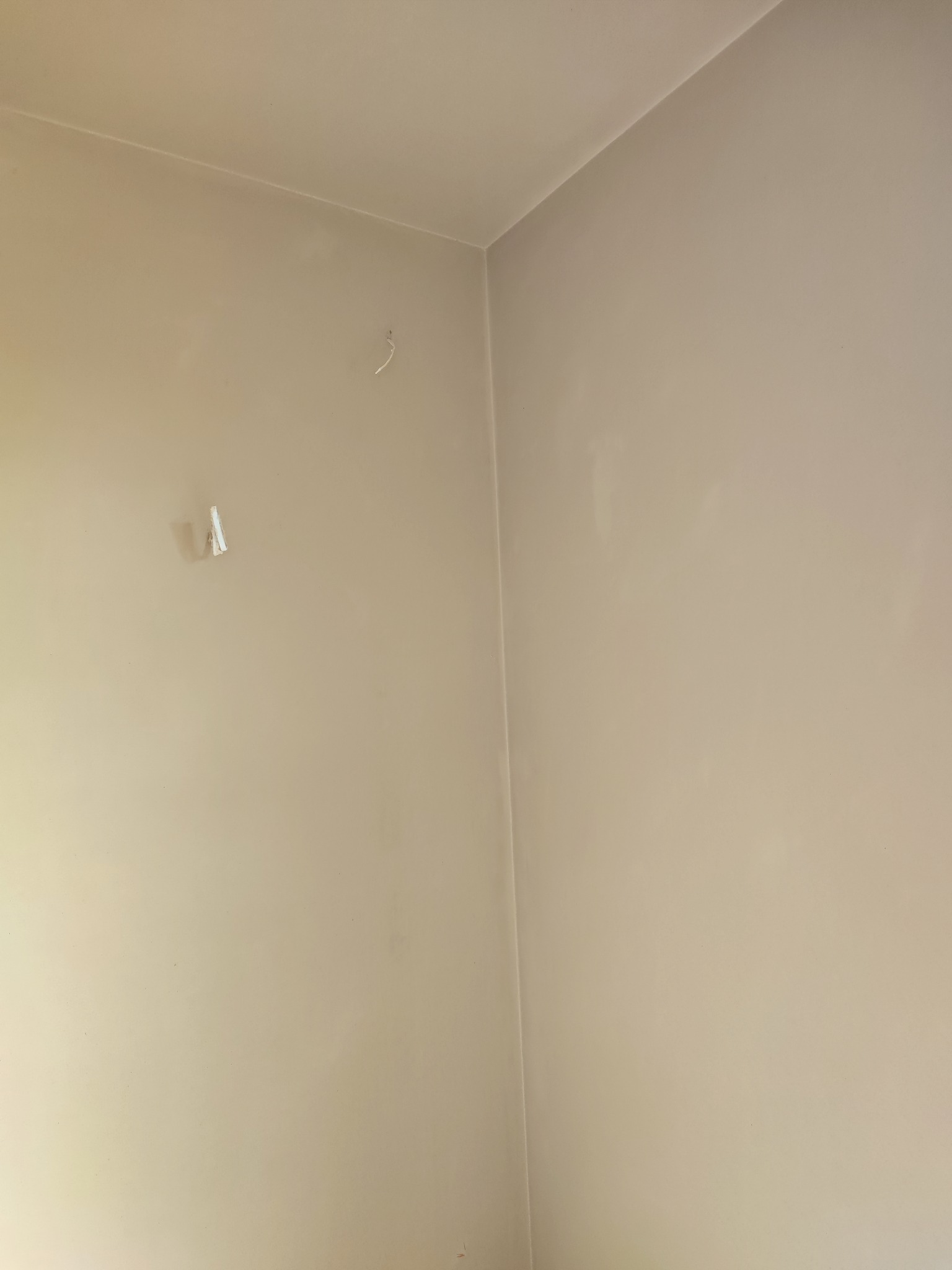 Świeżo pomalowany narożnik pokoju z widocznymi pozostałościami po taśmie malarskiej i wystającym kablem ze ściany.