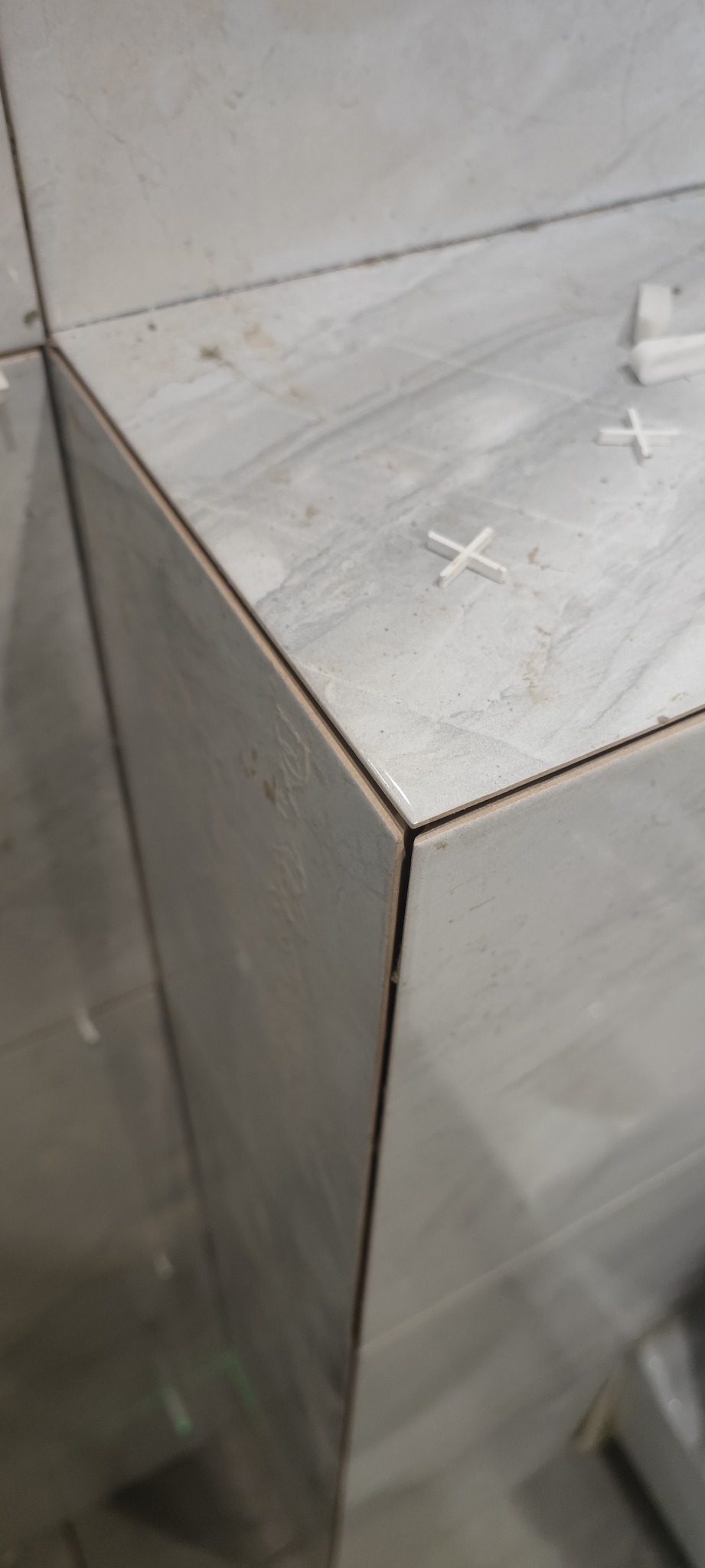 Układanie płytek imitujących marmur na narożniku, widoczne krzyżyki dystansowe i cienka fuga.