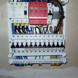 Rozdzielnica elektryczna z zabezpieczeniami przepięciowymi ELS, zamontowana na ścianie, widoczne różnokolorowe przewody i bezpieczniki IDEAL.