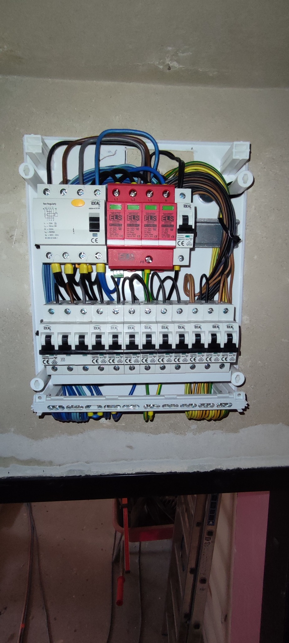 Rozdzielnica elektryczna z zabezpieczeniami przepięciowymi ELS, zamontowana na ścianie, widoczne różnokolorowe przewody i bezpieczniki IDEAL.