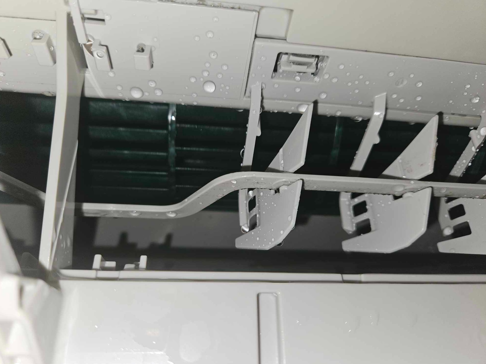 Wnętrze klimatyzatora z widocznymi elementami konstrukcyjnymi i skroploną wodą na powierzchni, sugerujące niedawne czyszczenie lub kondensację.