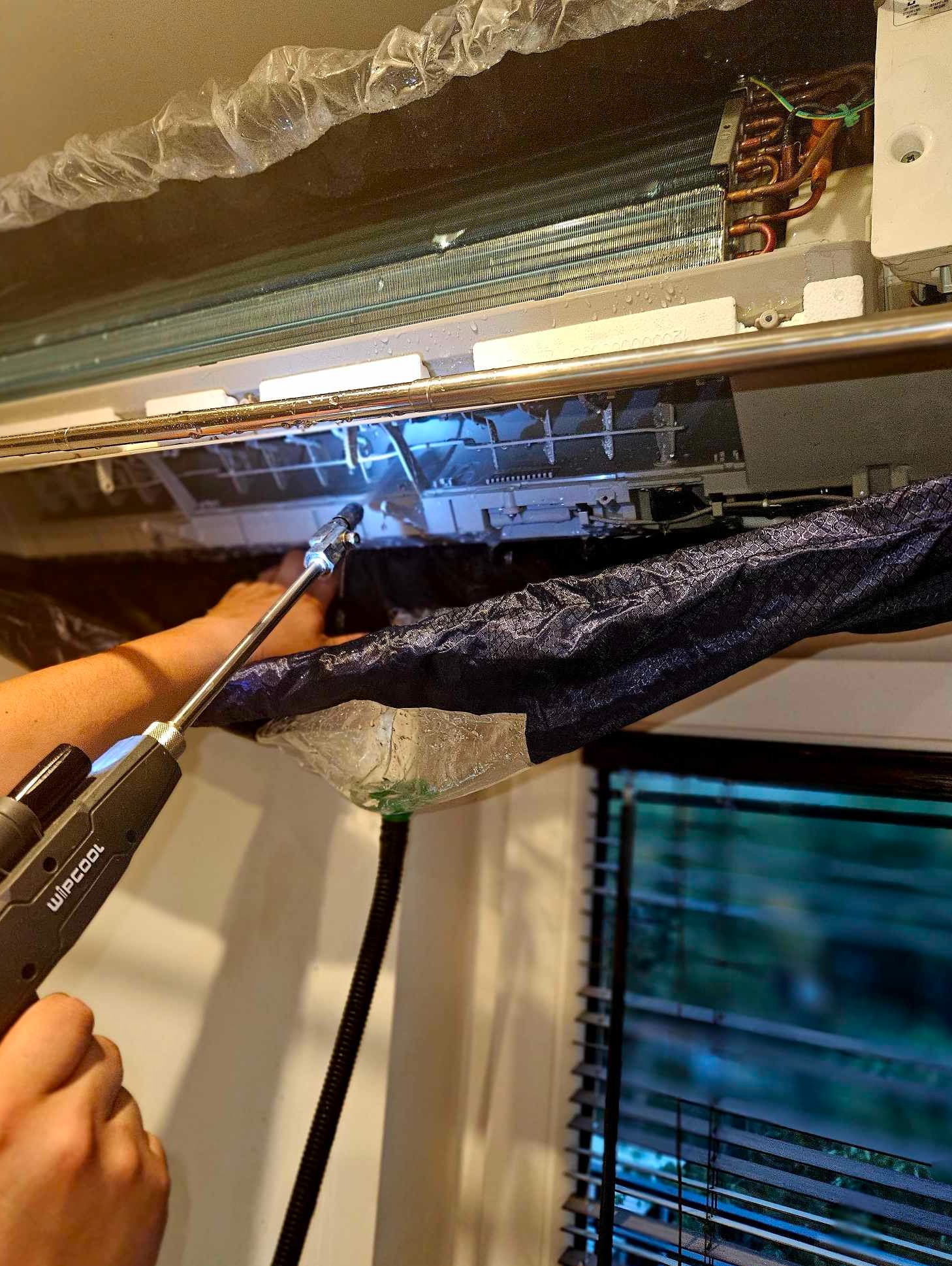 Czyszczenie wnętrza klimatyzatora za pomocą dyszy ciśnieniowej i specjalnego worka zbierającego zanieczyszczenia, widoczne mokre elementy urządzenia.