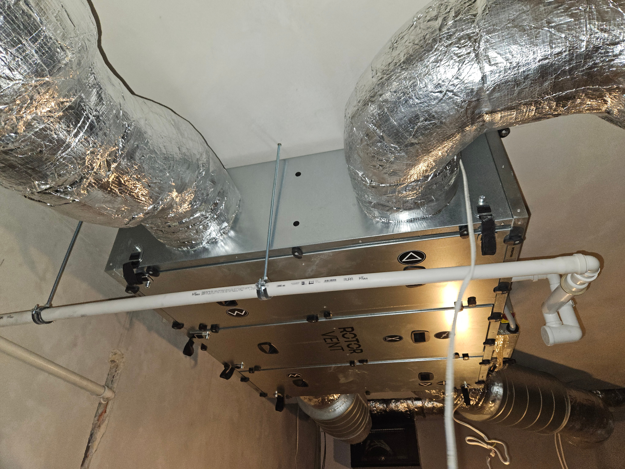 Zamontowana centrala wentylacyjna Rotor Vent z izolowanymi przewodami w pomieszczeniu, widok z dołu na sufit. Elementy instalacji widoczne w kadrze.