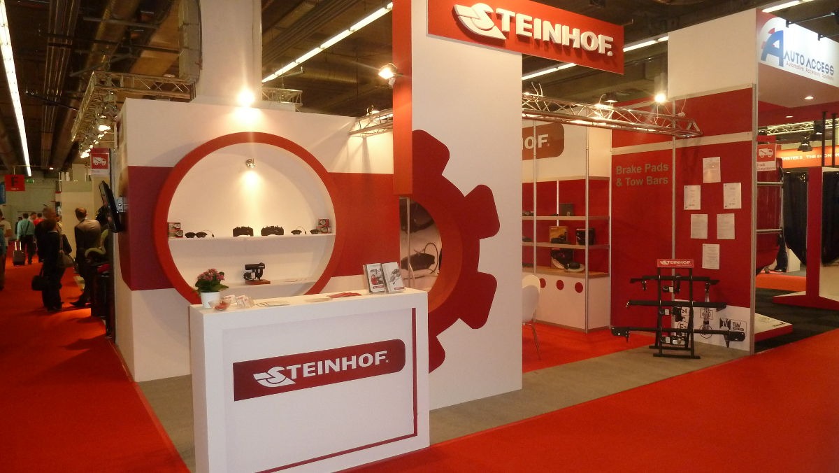 Stoisko targowe firmy Steinhof z czerwonymi akcentami, prezentujące akcesoria samochodowe, w tle widoczni ludzie.