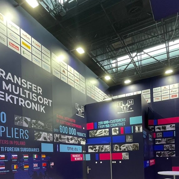 Stoisko targowe firmy z branży elektronicznej z logo TME, prezentujące informacje o globalnej dystrybucji komponentów, liczbie klientów i krajów, z licznymi logotypami partnerów na ścianie.
