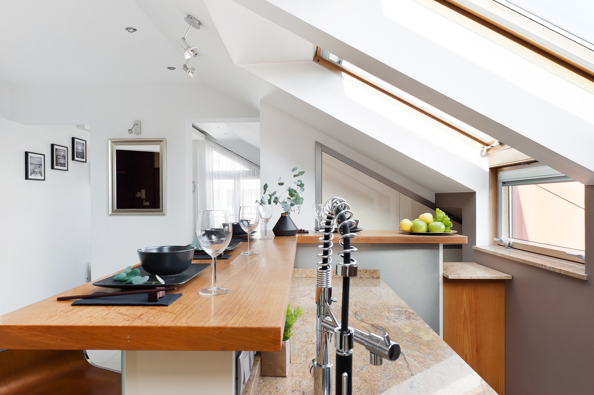 Nowoczesna kuchnia na poddaszu z drewnianym blatem, chromowaną baterią i oknem dachowym wpuszczającym dużo światła.