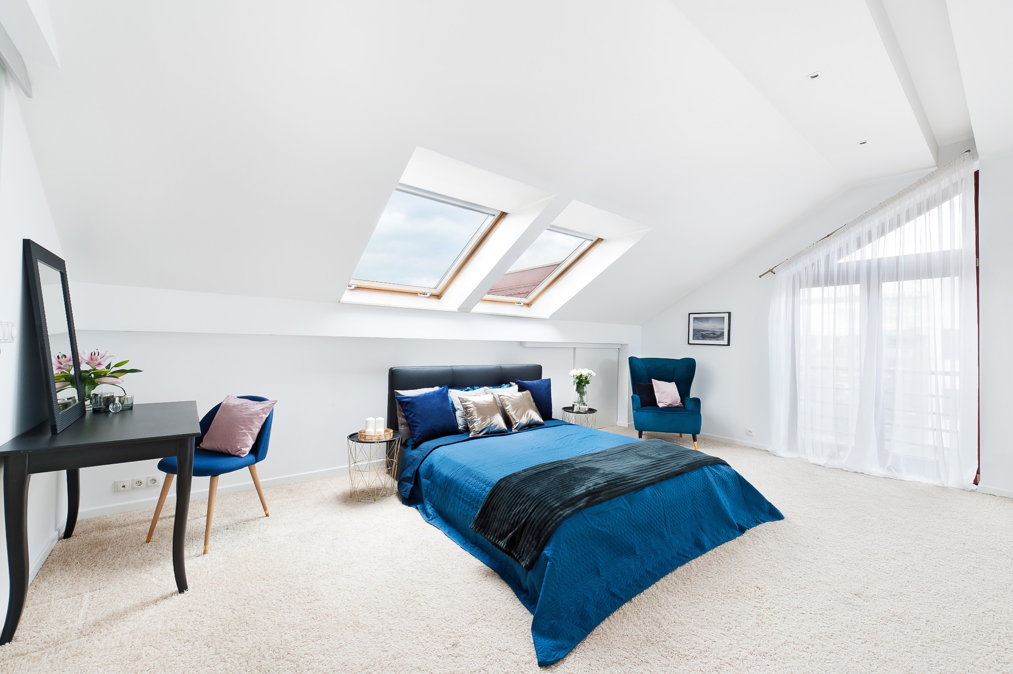 Jasne, przestronne poddasze z łóżkiem w odcieniach niebieskiego, biurkiem z lustrem i oknami dachowymi