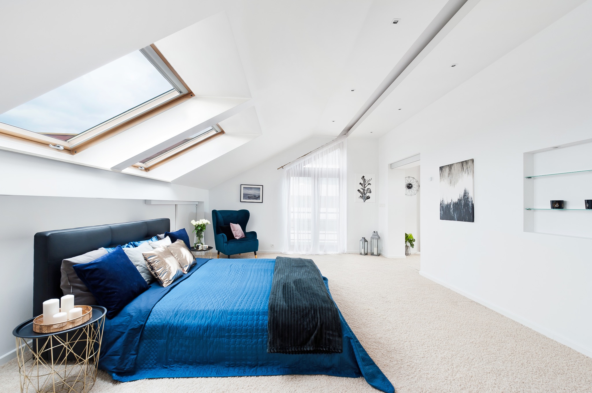 Jasne, przestronne poddasze z łóżkiem w kolorze granatowym, oknami dachowymi i turkusowym fotelem uszakiem