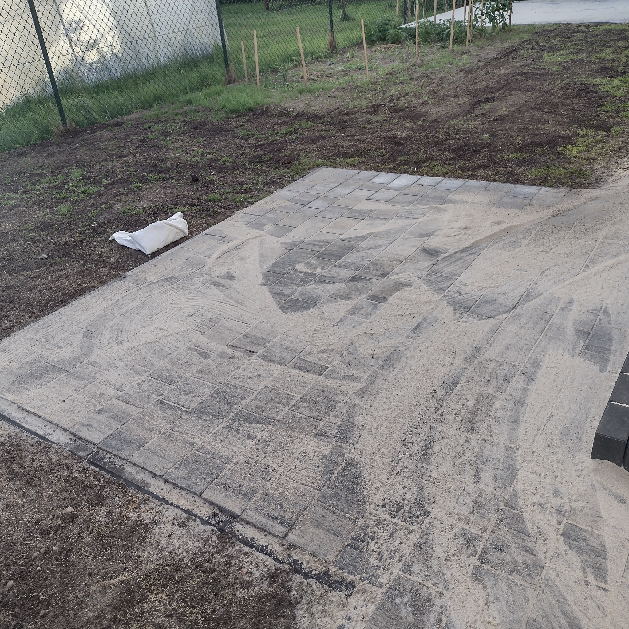 Fragment układanej szarej kostki brukowej w Łodzi, z widocznym workiem z piaskiem obok i świeżo obsypaną piaskiem powierzchnią.