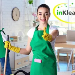 Zespół sprzątający w akcji: uśmiechnięta kobieta w centrum kadru, z uniesionym kciukiem, ubrana w zielony fartuch i żółte rękawice, w tle mężczyzna odkurzający sofę i kobieta ścierająca kurz...