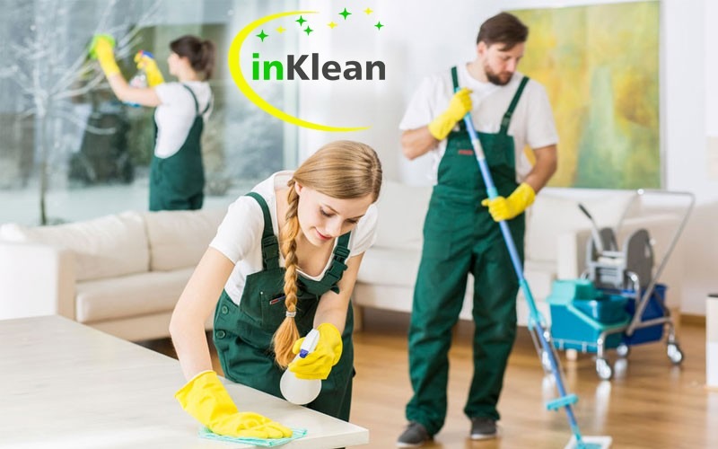 Zespół sprzątający inKlean w akcji: kobieta czyści blat, mężczyzna myje podłogę mopem, a trzecia osoba myje okno, wszyscy w zielonych kombinezonach i żółtych rękawicach.