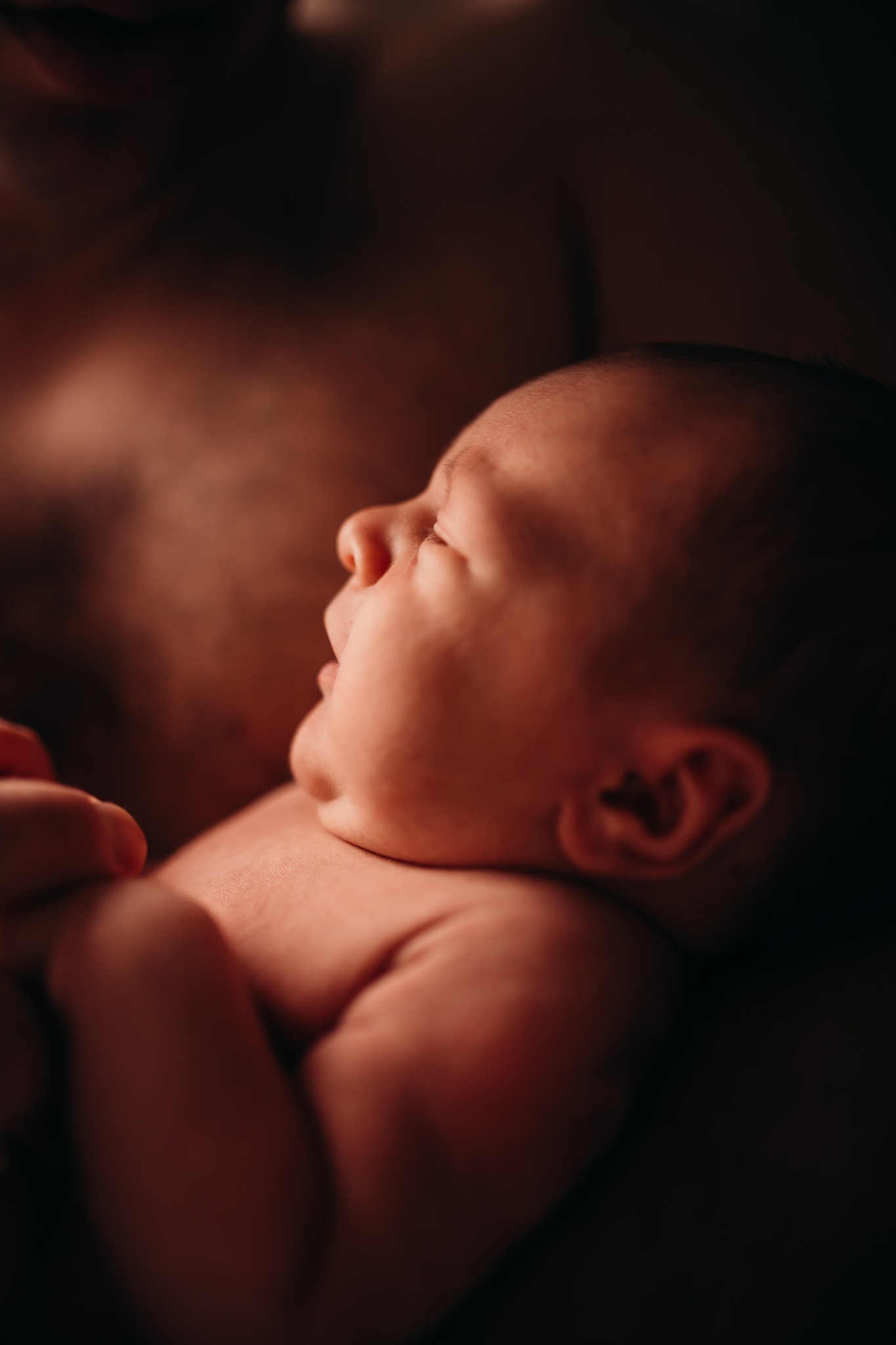 Profil śpiącego noworodka w ramionach rodzica, delikatne oświetlenie podkreśla rysy twarzy i fakturę skóry.