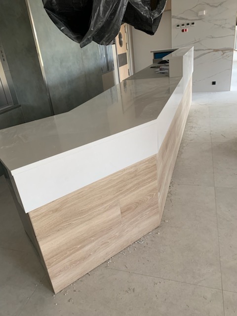 Błyszczący blat kamienny o nieregularnym kształcie z drewnopodobnym wykończeniem frontu, widoczny w surowym wnętrzu w trakcie prac wykończeniowych.