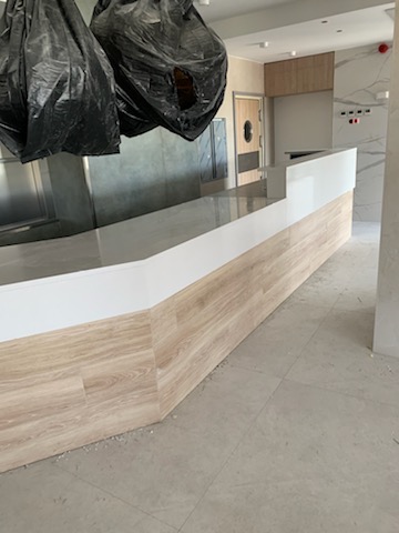 Wnętrze w trakcie wykańczania z długim blatem z białego konglomeratu i okładziną imitującą drewno na podstawie, widoczne worki z odpadami budowlanymi.