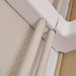 Sun House 🌞 - Fragment instalacji grzewczej z drewnianymi rurami wchodzącymi w białą, metalową obudowę.