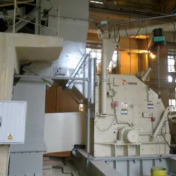 Beżowa, przemysłowa maszyna Metso zamontowana na stalowej konstrukcji, z widocznymi elementami instalacji elektrycznej i żółtym wiadrem na podłodze.