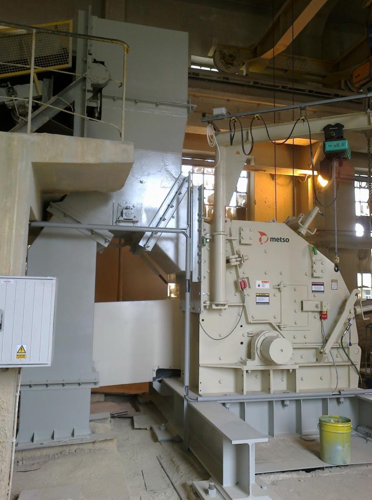 Beżowa, przemysłowa maszyna Metso zamontowana na stalowej konstrukcji, z widocznymi elementami instalacji elektrycznej i żółtym wiadrem na podłodze.