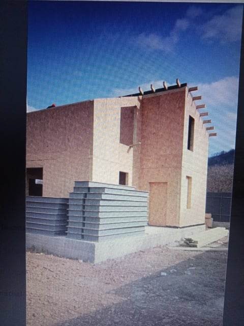 Surowy stan dwukondygnacyjnego domu szkieletowego z widocznymi panelami izolacyjnymi na fundamencie, w tle błękitne niebo.