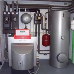 Kompaktowa kotłownia w piwnicy z kotłem Viessmann Vitola 200, zasobnikiem ciepłej wody, pompami obiegowymi i rozbudowaną instalacją rur w izolacji.