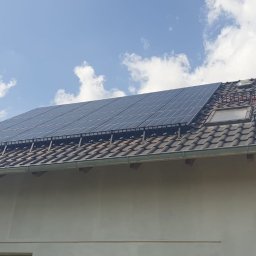 ElektroGriner - Panele fotowoltaiczne na dachu domu jednorodzinnego, widoczne rusztowania i okna dachowe. Błękitne niebo z chmurami w tle.