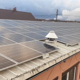 ElektroGriner - Instalacja fotowoltaiczna na dachu budynku z kominkami wentylacyjnymi, widok z góry, pochmurne niebo w tle.