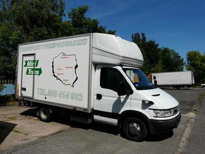 Biały samochód dostawczy z napisem 'Transport/Przeprowadzki' i mapą Polski z zaznaczonymi miastami, zaparkowany na placu.