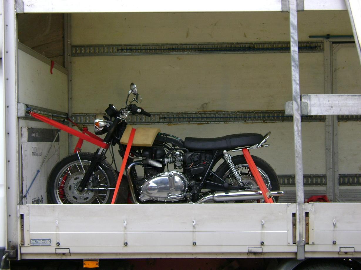 Motocykl zabezpieczony czerwonymi pasami transportowymi wewnątrz przestrzeni ładunkowej pojazdu.