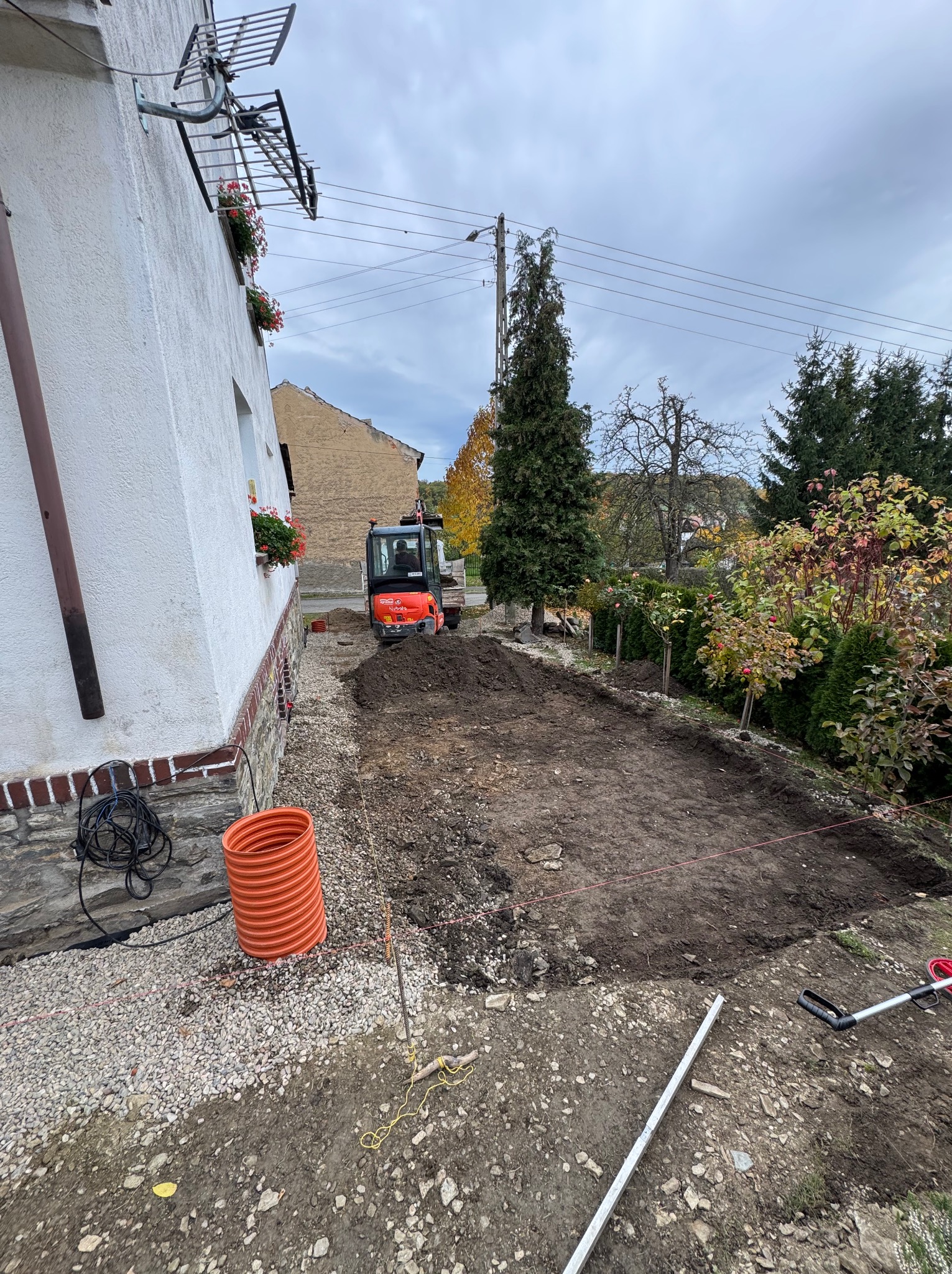 Teren przygotowany pod budowę, widoczny mały traktor, rura kanalizacyjna i narzędzia. Wykop pod przyszłą inwestycję na działce przy domu.