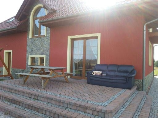 Czerwony dom jednorodzinny z kamienną elewacją, drewnianym stołem piknikowym i czarną skórzaną sofą na brukowanym tarasie.