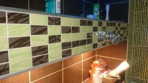 Fragment wykończonej łazienki z mozaiką z płytek w odcieniach brązu i zieleni, widoczna bateria umywalkowa i akcesoria łazienkowe.