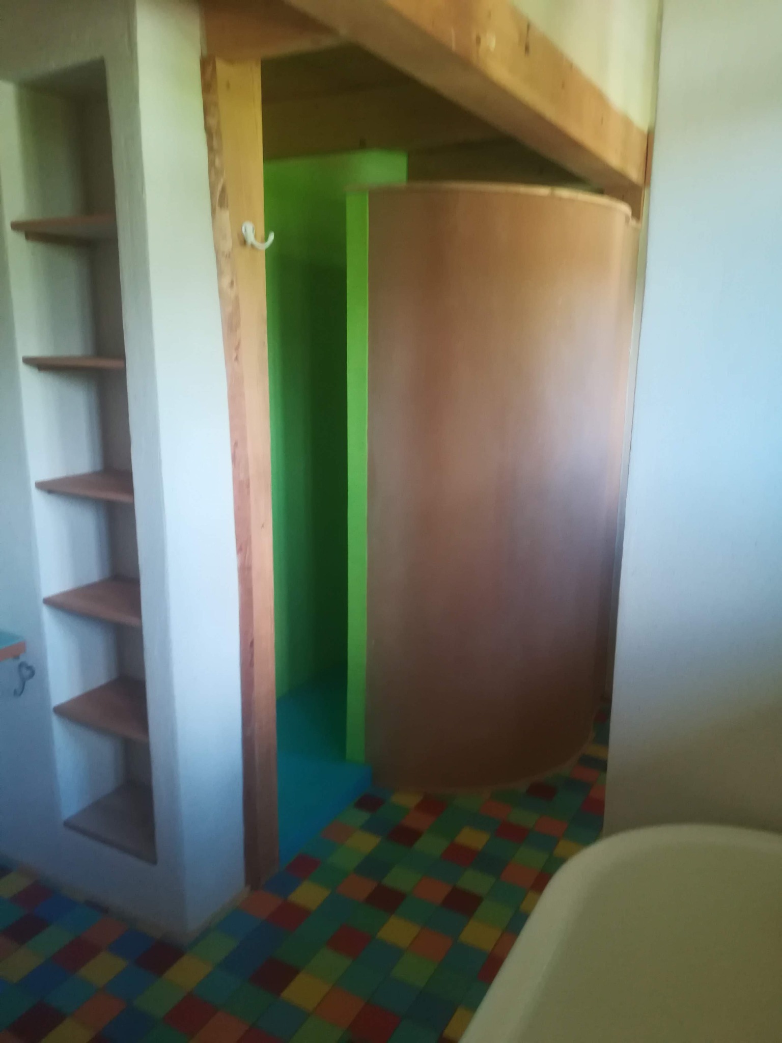 Niedokończona łazienka z kolorową podłogą, półkami w ścianie i zaokrągloną ścianą kabiny prysznicowej w trakcie montażu.