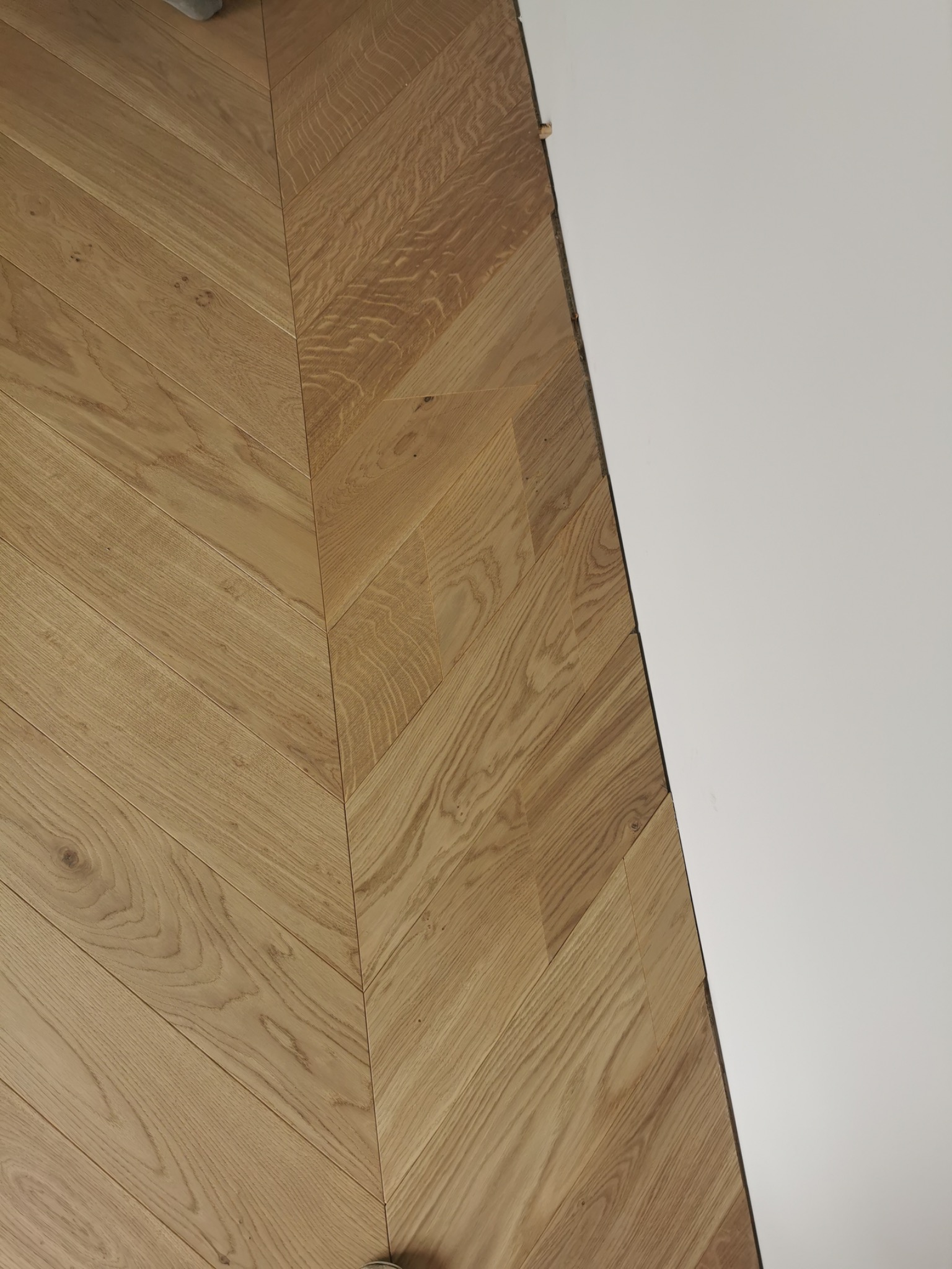 Ułożony parkiet w jodełkę francuską z jasnego drewna, widoczna ściana w kolorze białym.