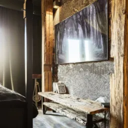 Nowoczesny salon z telewizorem na ścianie o surowej fakturze, drewniane belki konstrukcyjne i stolik z odzyskanego drewna, oświetlenie punktowe.